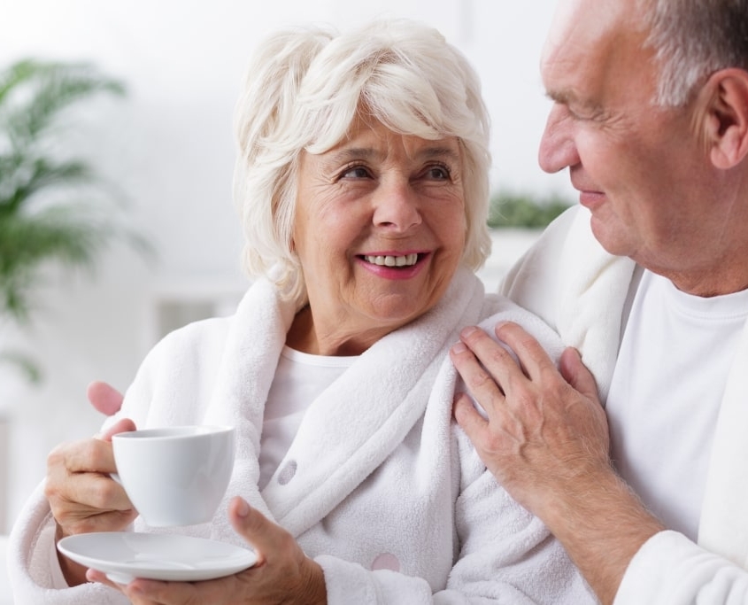 Ouder koppel in een witte badjas genieten samen van een kopje thee of koffie.